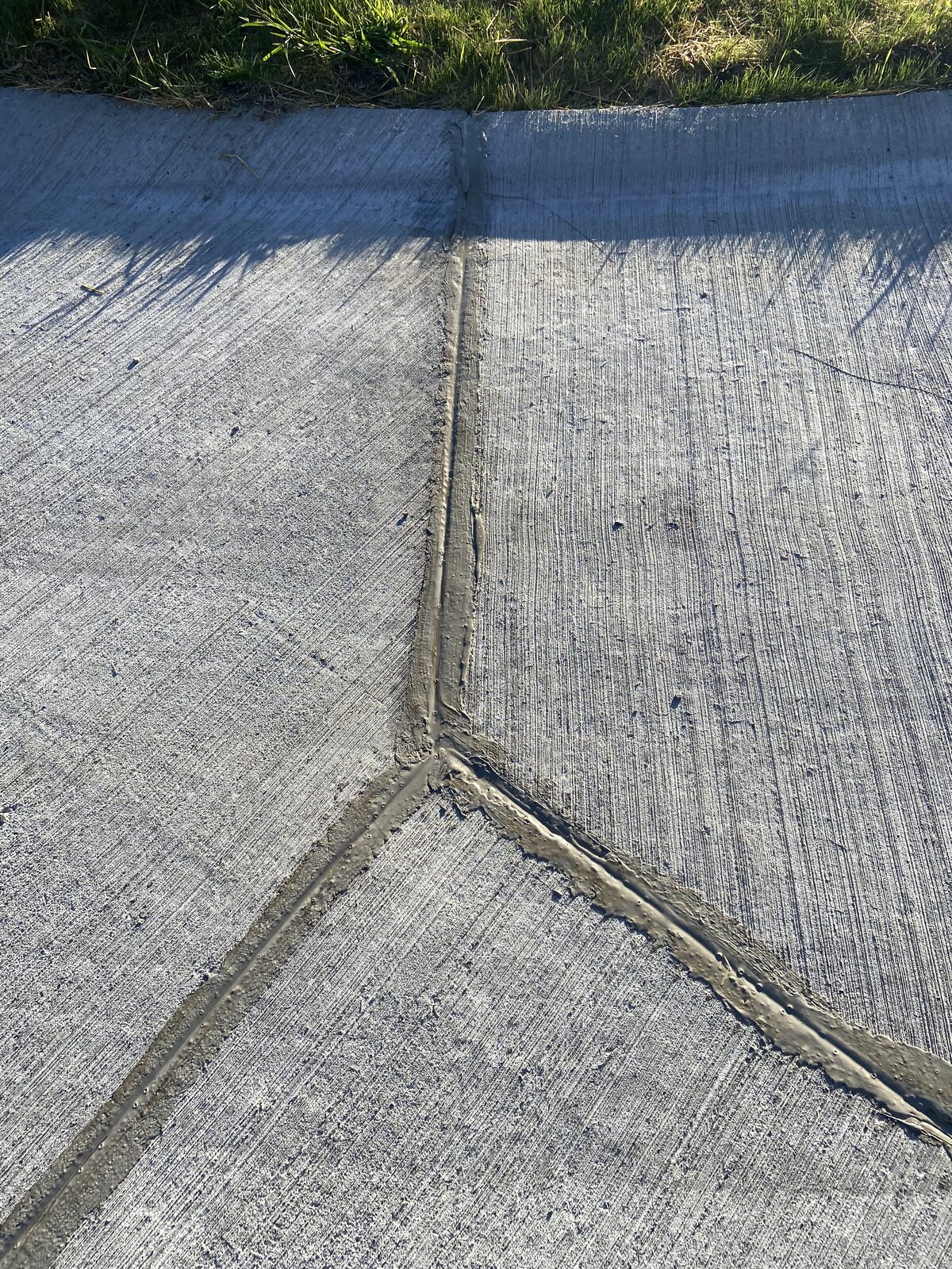 Gray Crack Seal V-shaped joint repair on concrete driveway by Asphalt Fabrics & Specialties — no black asphalt lines
